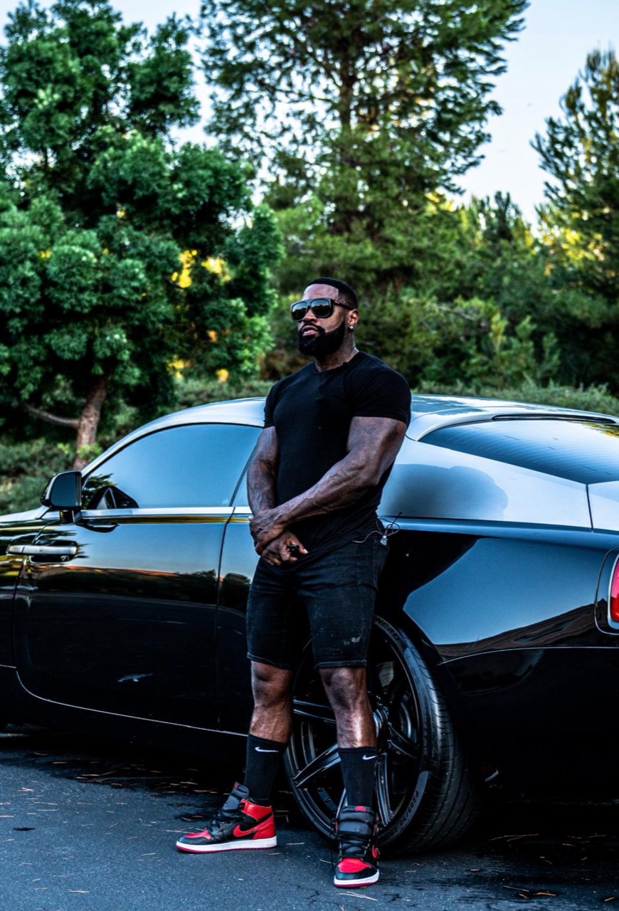 Mike Rashid standing beside a dark car with tall trees behind him