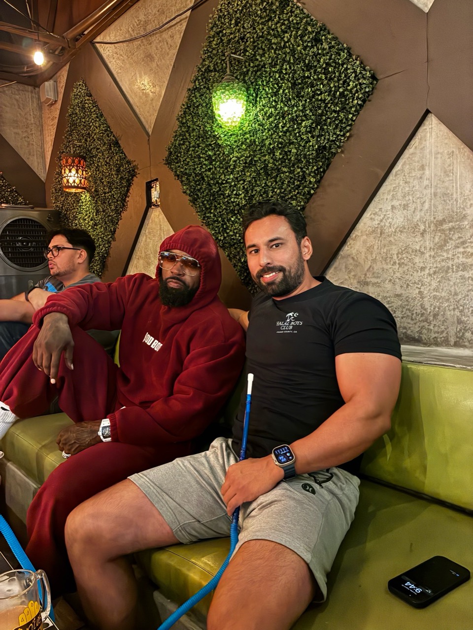 Mike Rashid in a red hoodie seated beside a companion on a green sofa