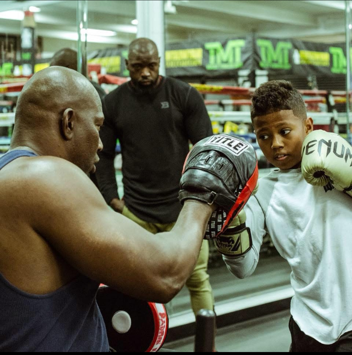 A young boxer practicing with focus mitts while an adult watches the session