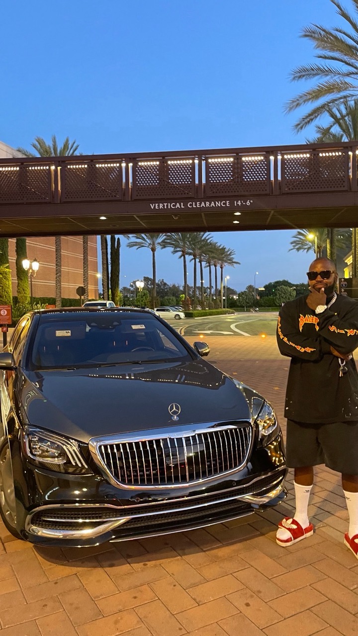 Mike Rashid standing beside a dark Mercedes at dusk, with palm trees in the background