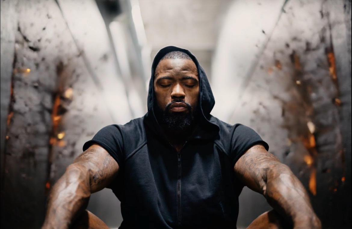 Mike Rashid seated with his eyes closed, wearing a black sleeveless hoodie